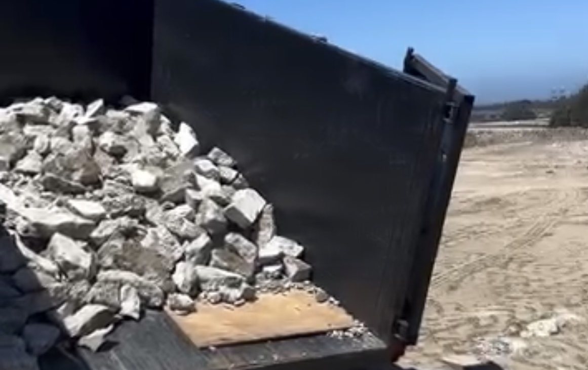 Broken concrete and construction debris loaded into a Monterey Bay Junk Services dump trailer on a job site