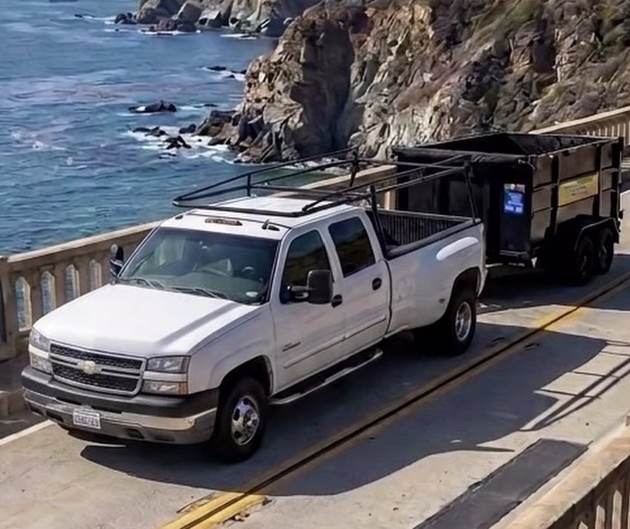 Monterey Bay Junk Services pickup towing a loaded dump trailer across a bridge on the Big Sur coast